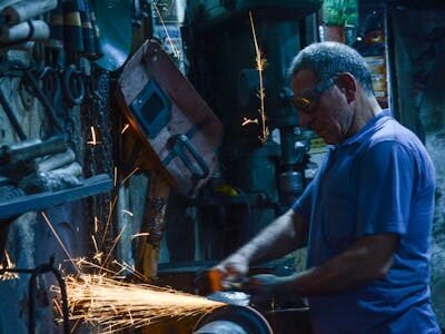 Experienced metal worker using a grinder, creating sparks in a busy workshop setting.