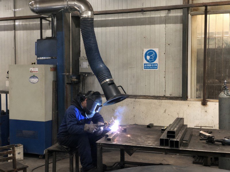 Welder working under a fume extraction hood in an industrial workshop